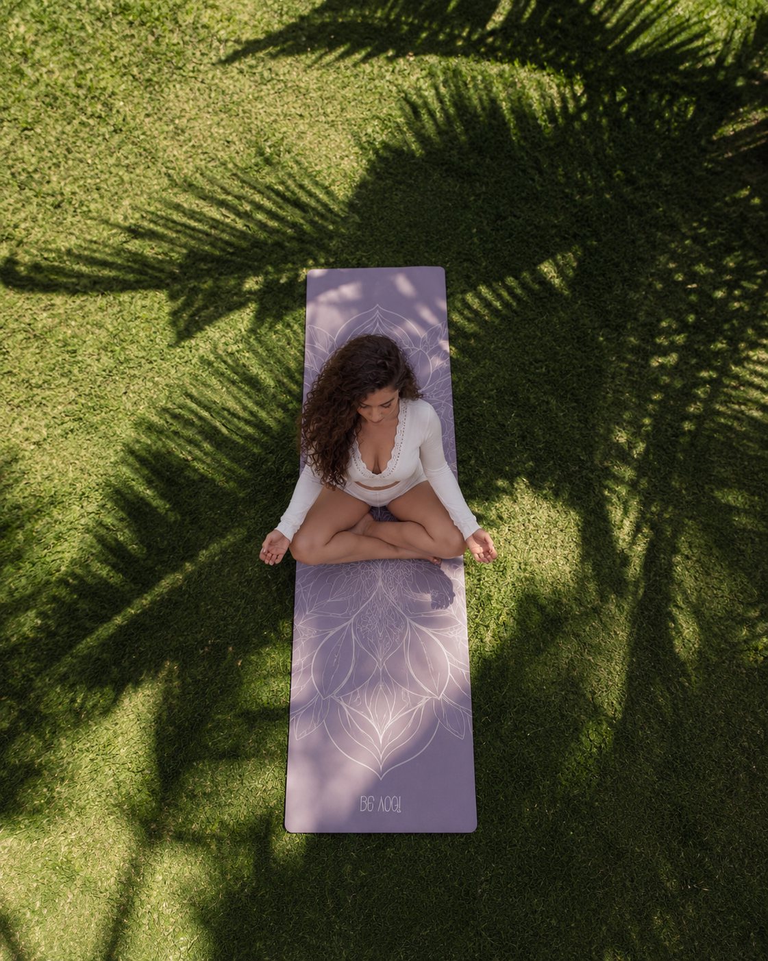 Mujer meditando sobre un mat, vista aérea entre sombras de hojas